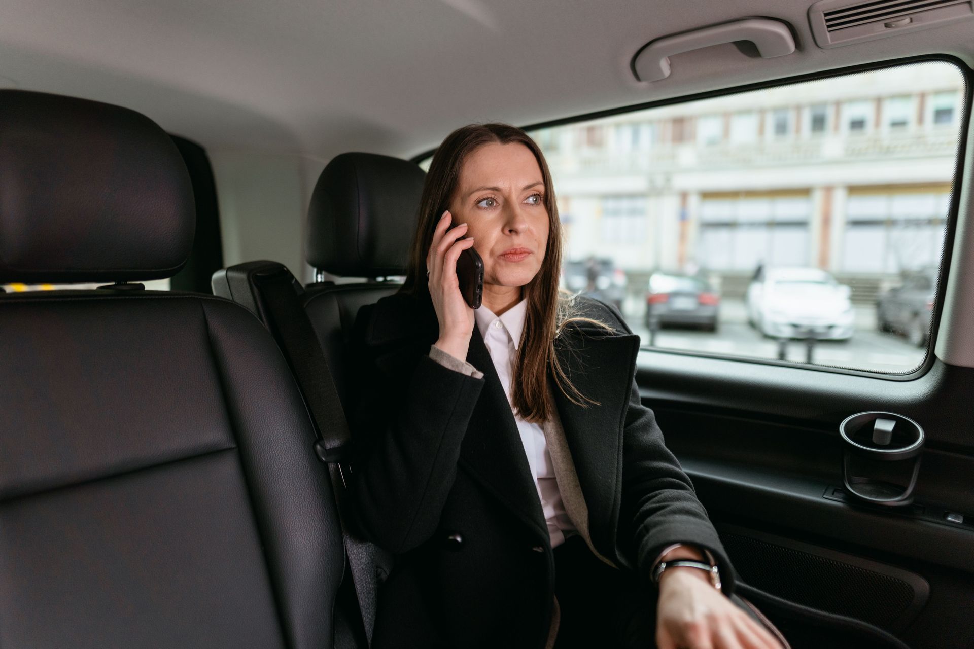 Professional woman in a car, engaged in a phone call, emphasizing communication and business.